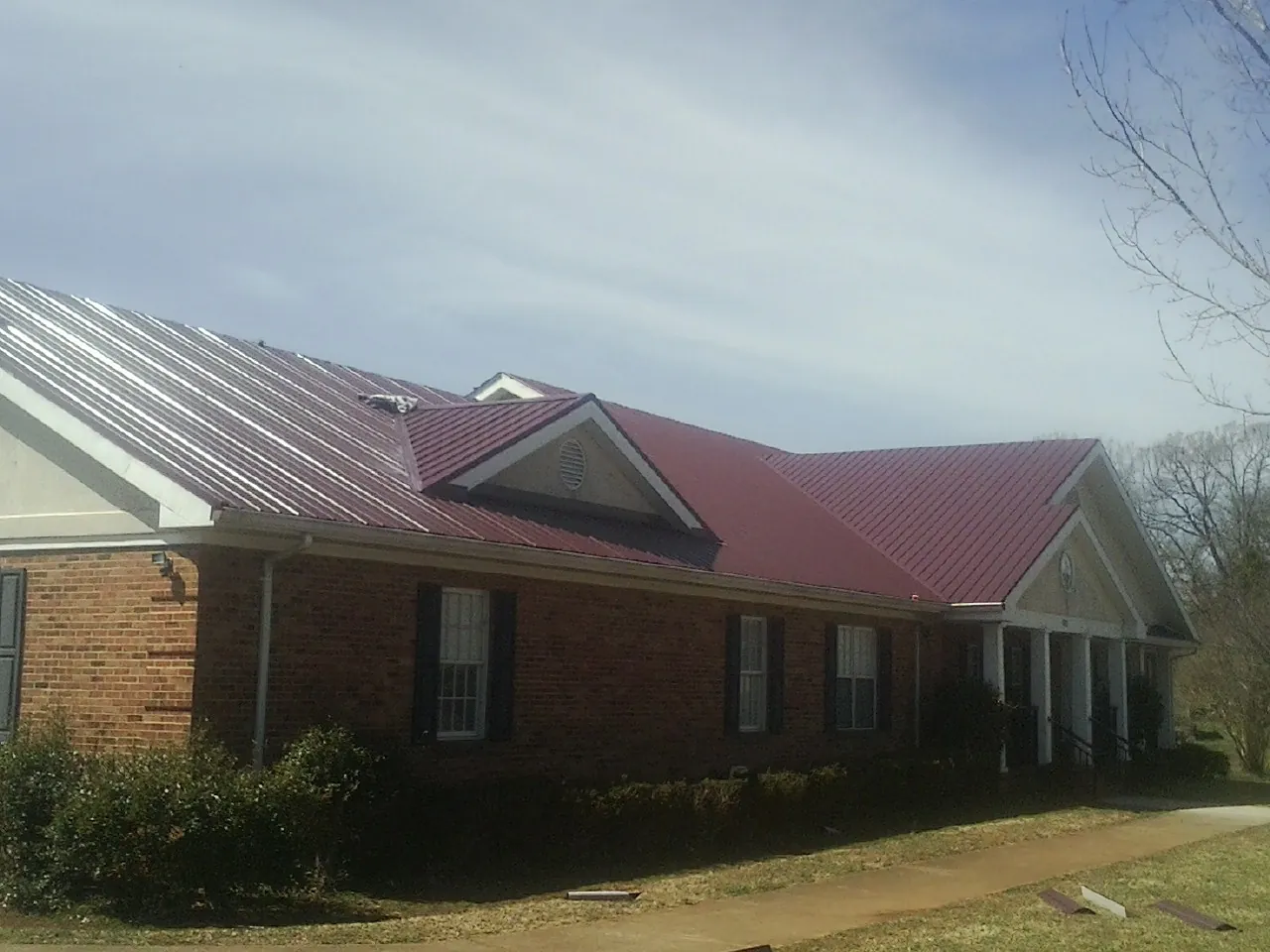 Red metal roof with gabled entries on a long brick building, from a Hail Damage Roof Repair job in Semmes