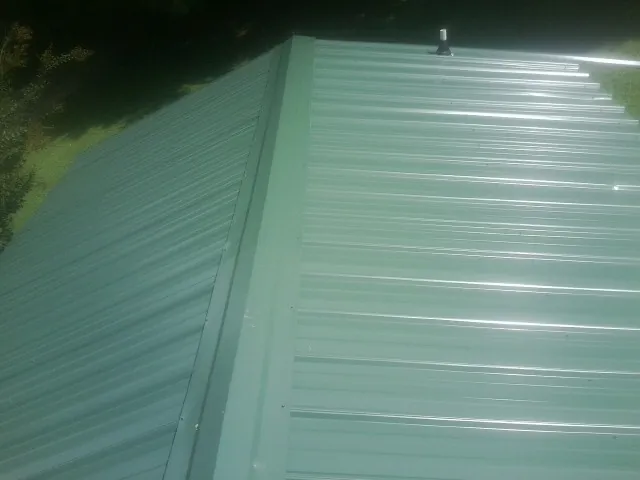 New green metal panels meeting at the ridge of a roof — Flat Roof Repair work by our crew in Semmes