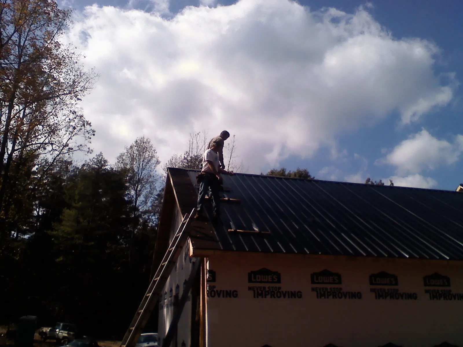 Roofer fastening dark metal panels high against a cloudy sky, from a Roof Inspection job in Semmes