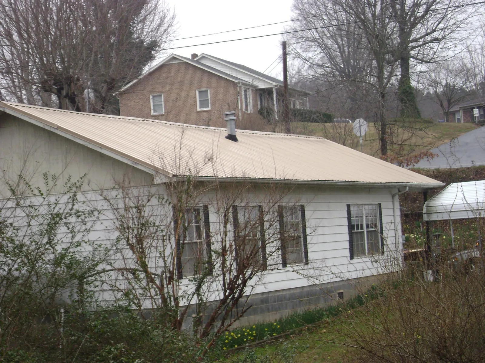 Tan metal roof on a white sided house set into a hillside — Commercial Roofing by Roofing Brothers in Semmes
